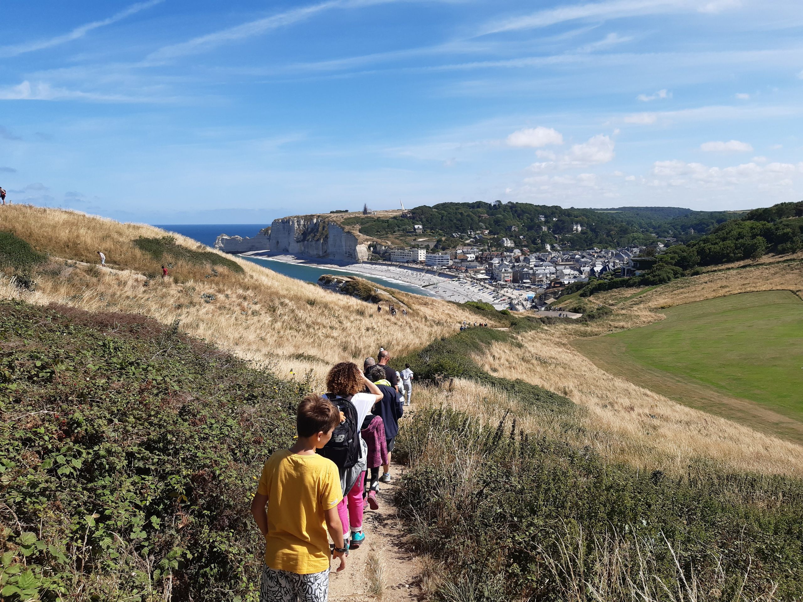 Wycieczki szkolne 9 A group hiking along a trail overlooking Étretat cliffs and town, Normandy, France.