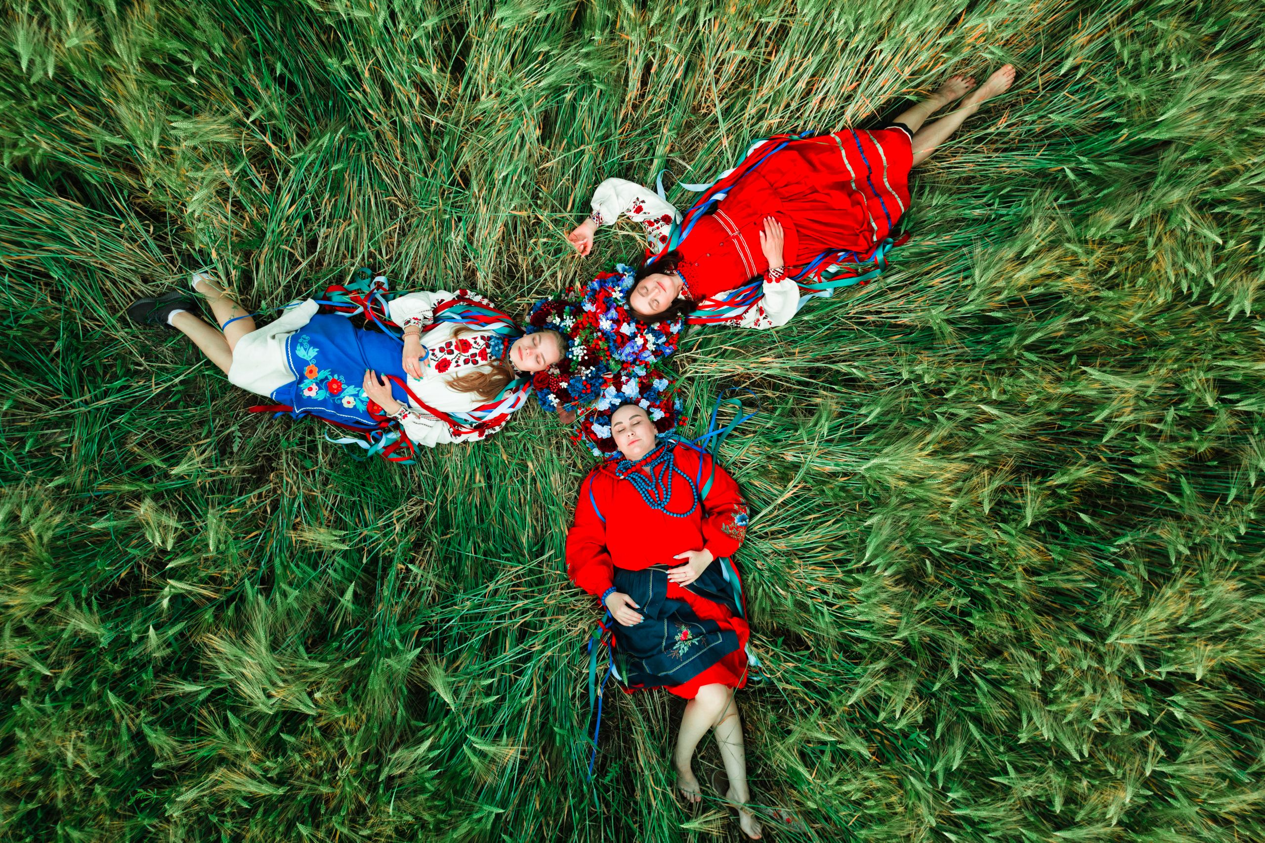 Oferty dla grup 10 Aerial view of women in vibrant traditional dresses lying together on a grass field.