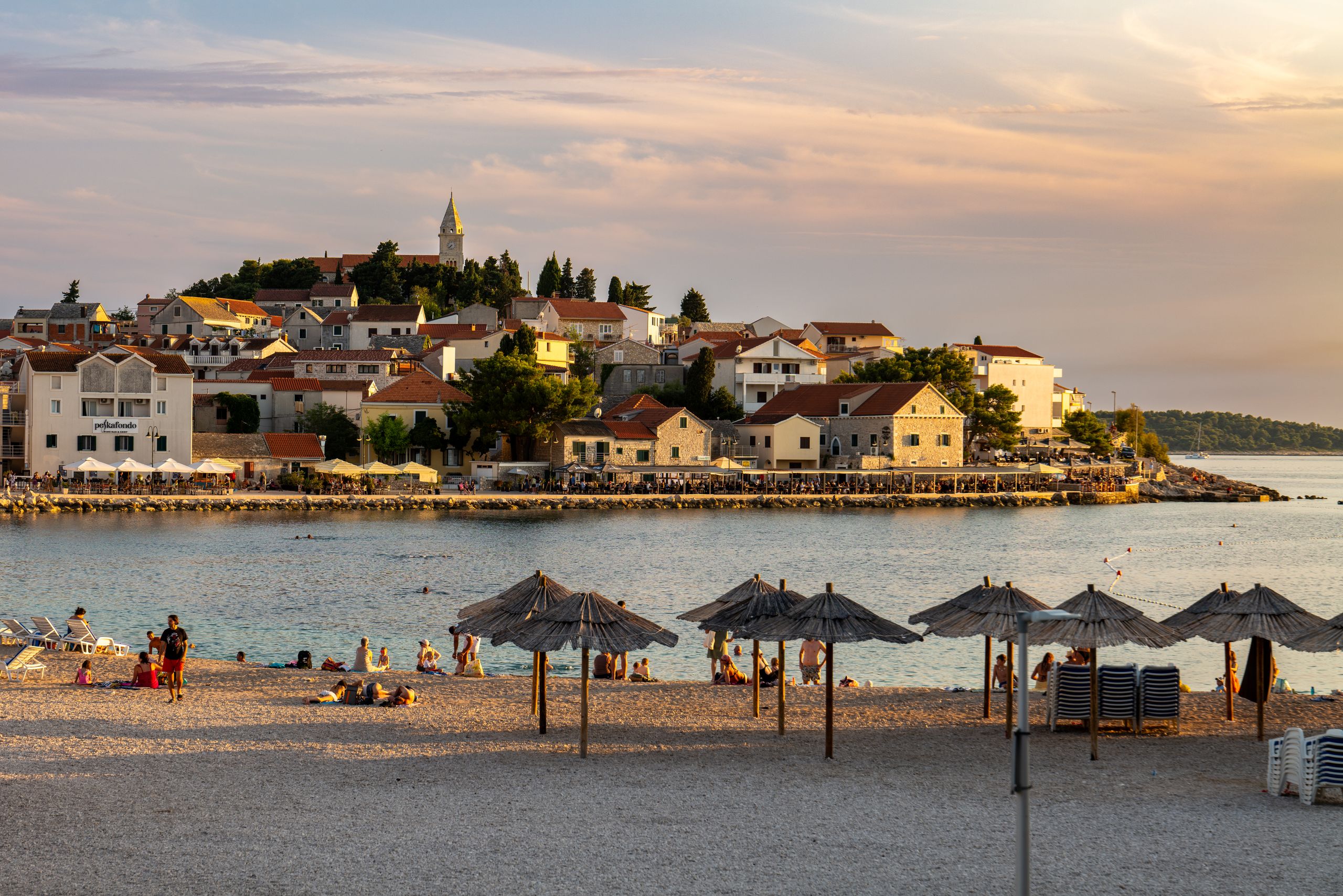Wczasy i Wycieczki 9 Beautiful beach scene with town and umbrellas at sunset in Primošten, Croatia.