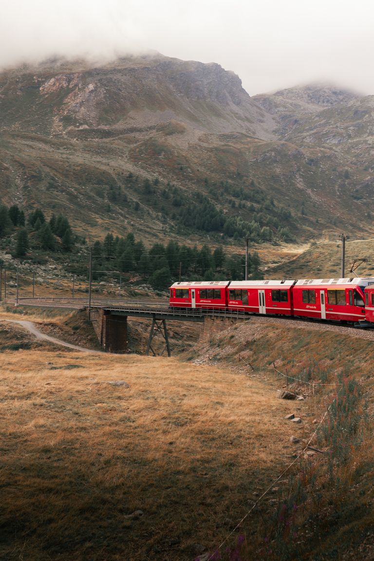 Strona główna 5 Captivating view of a red train traversing the majestic Swiss Alps in autumn near Saint Moritz.
