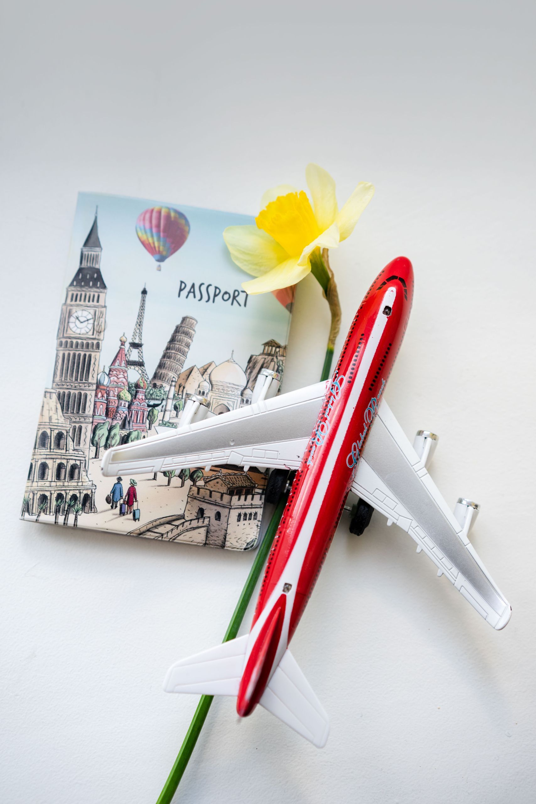 Flat lay of a toy airplane, passport, and flower, evoking travel themes.