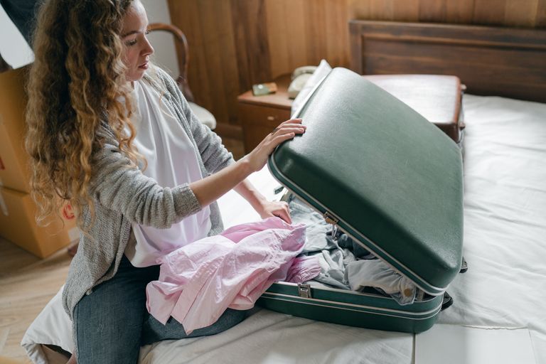 Strona główna 77 From above concentrated young female in casual wear with long curly hair sitting on bed and packing suitcase before trip