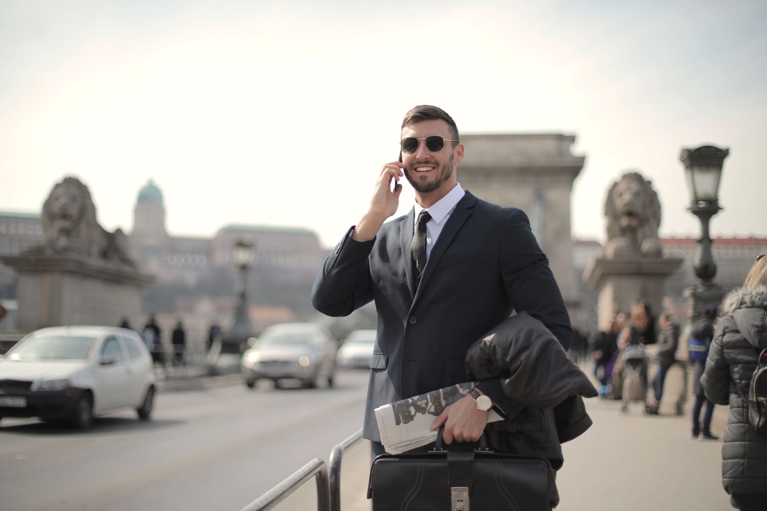 Oferty dla grup 6 Smiling businessman in formal attire using smartphone on a historic bridge.