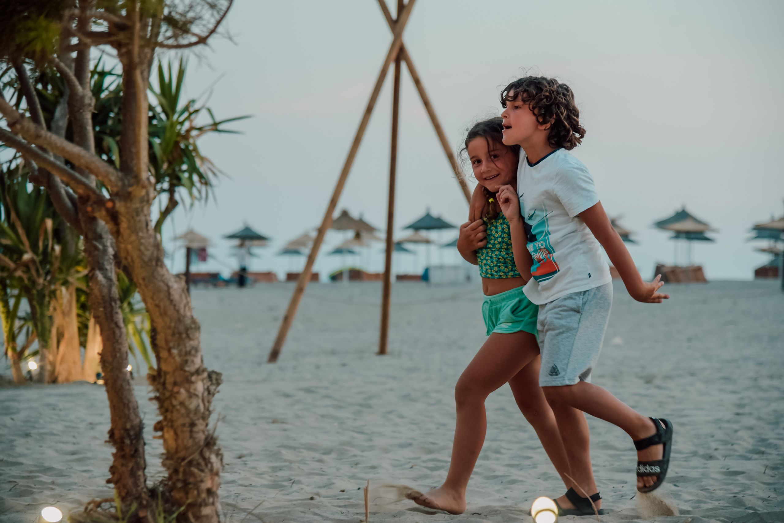 Wycieczki szkolne 3 Two children enjoy a playful walk on a sandy beach, capturing summer fun.