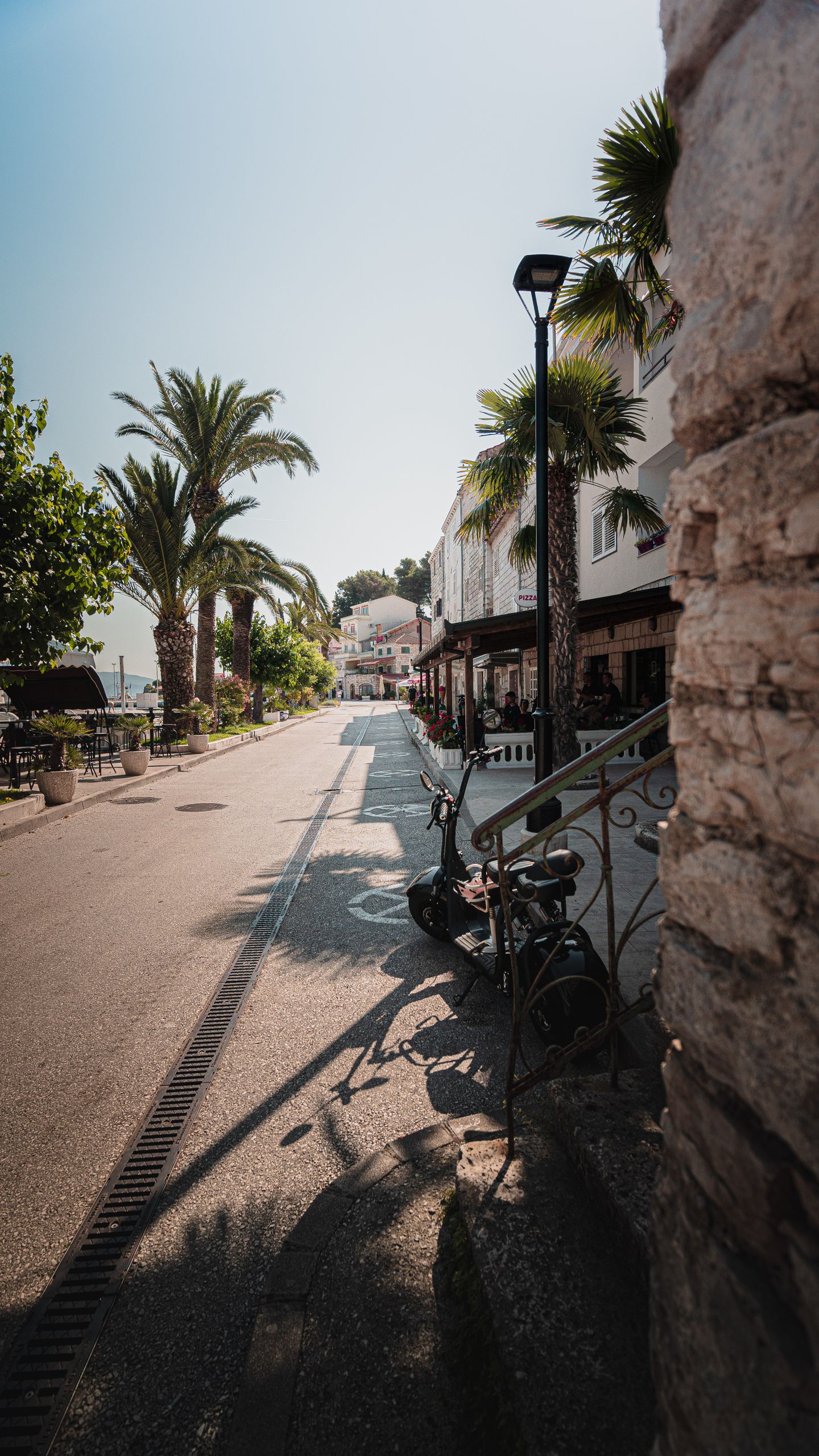 Wczasy i Wycieczki 2 Scenic city street with palm trees and cozy cafes, bathed in warm sunlight, perfect for urban exploration.