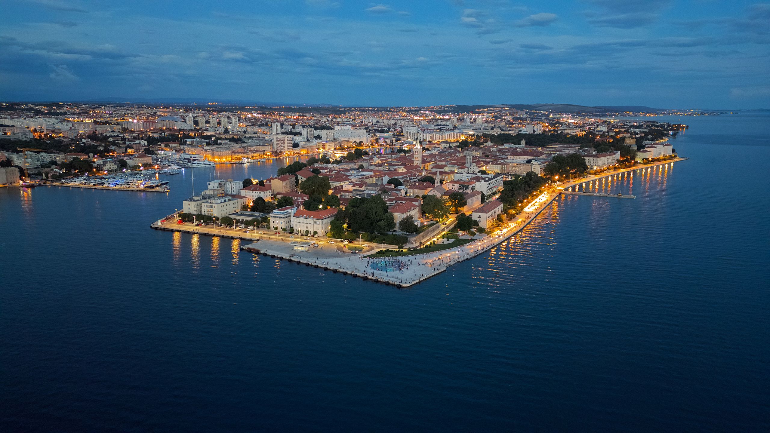Wczasy i Wycieczki 4 Stunning aerial view of Zadar's illuminated coast at twilight, showing the vibrant cityscape.